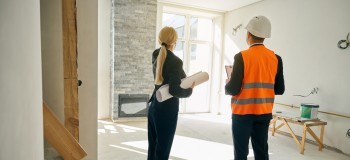 Female client and male engineer standing in room under construction