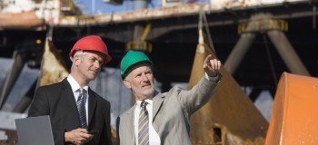 Two oil platform inspectors with a laptop, with the platform in the background 